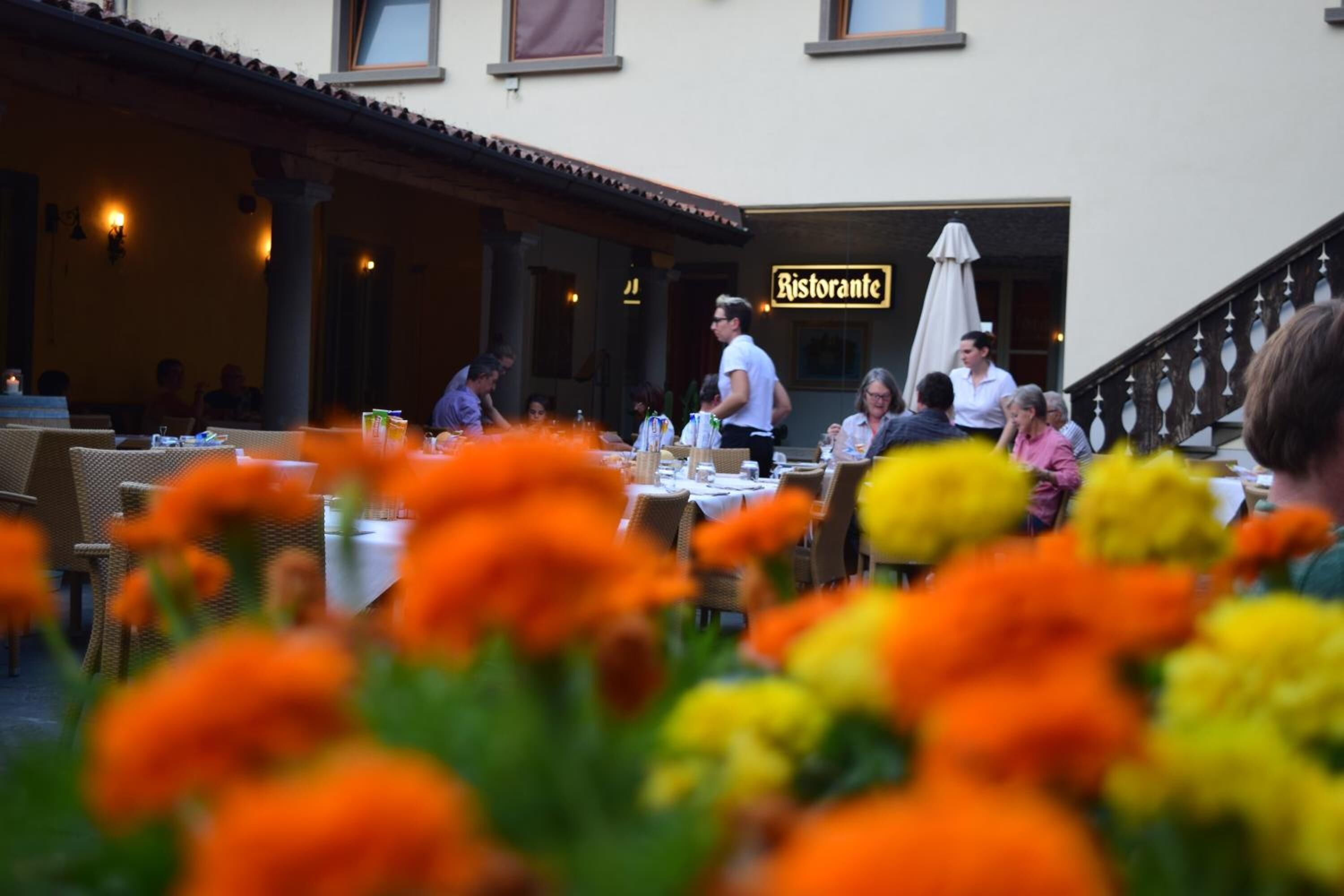 Un restaurante al aire libre con mesas y sillas, un letrero que dice "Ristorante" y una escalera que lleva a un nivel superior.