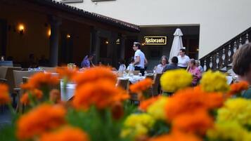Un restaurante al aire libre con mesas y sillas, un letrero que dice "Ristorante" y una escalera que lleva a un nivel superior.