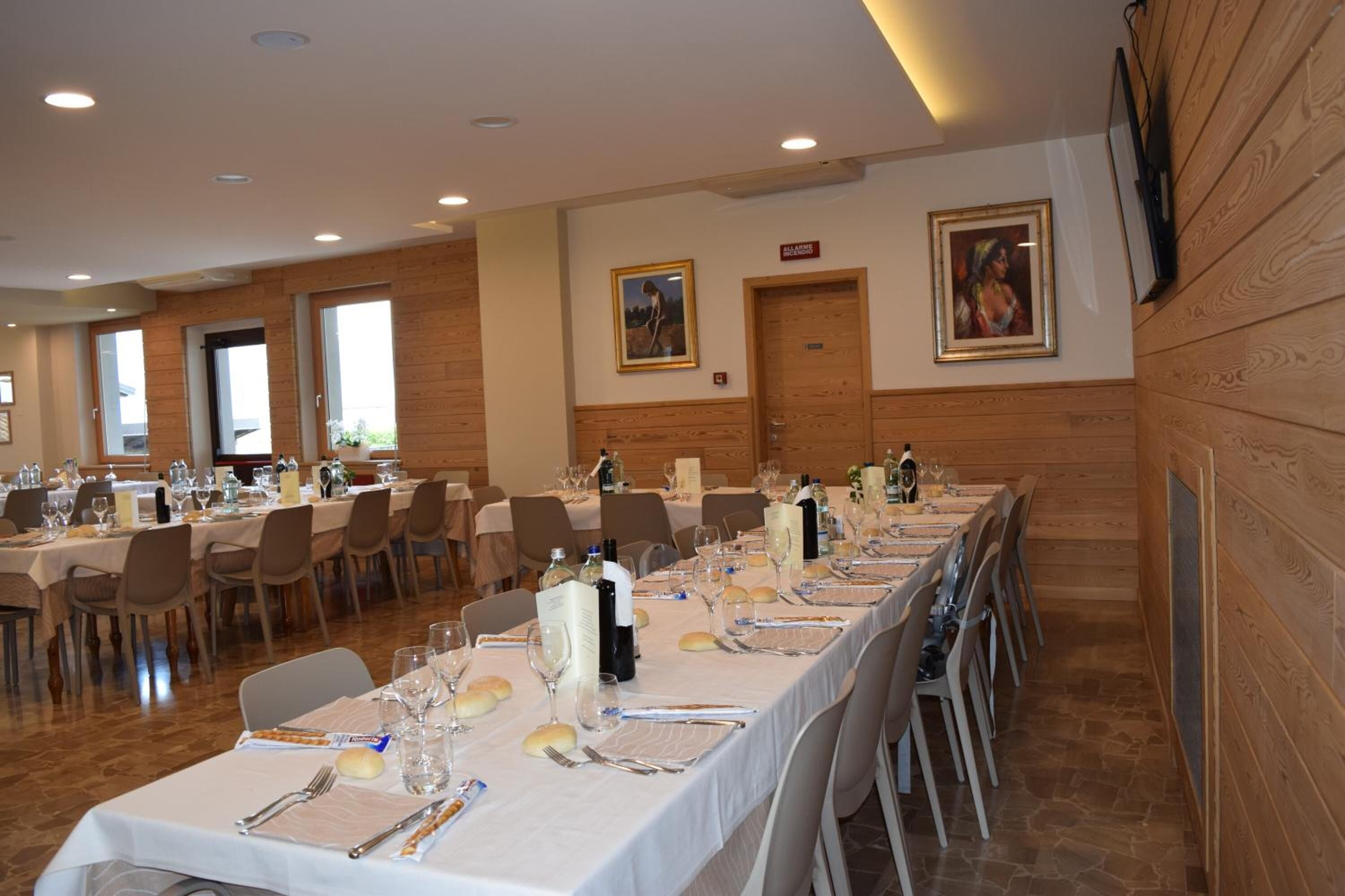 Una larga mesa de comedor dispuesta para un evento formal en una sala con paneles de madera y un cuadro grande en la pared.