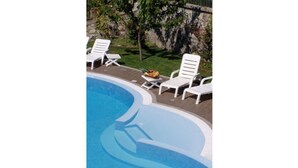 A swimming pool with white lounge chairs and a fruit bowl on the edge.