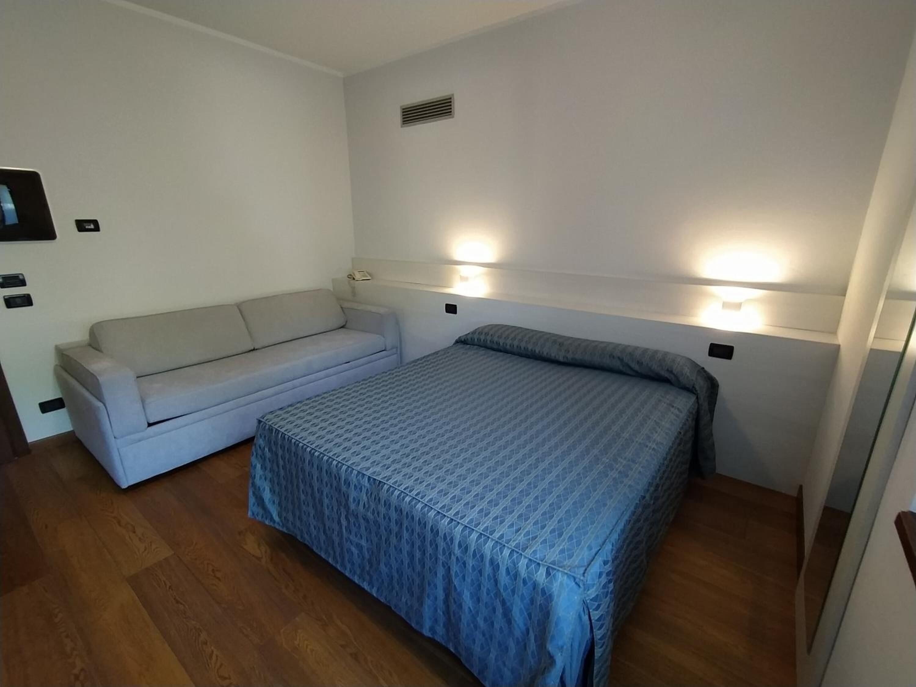 Una habitación pequeña y limpia con una cama, un sofá y dos luces fijadas a la pared.