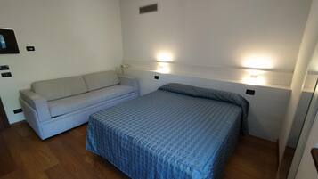 Una habitación pequeña y limpia con una cama, un sofá y dos luces fijadas a la pared.