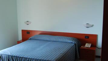 Una cama individual con cabecera de madera, una mesita de noche con teléfono, y una lámpara fijada a la pared.