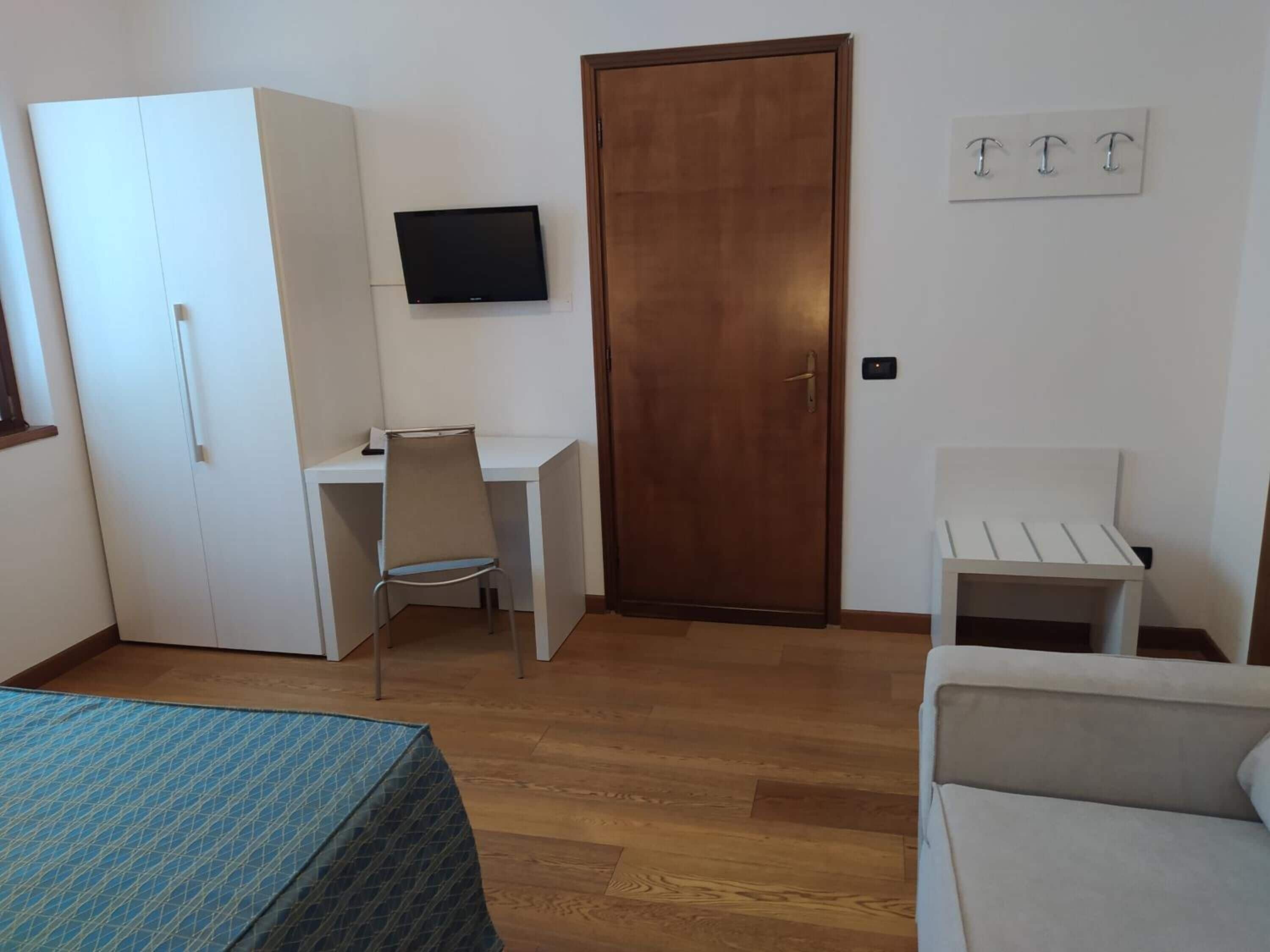 A room with a bed, a desk, a chair, a wardrobe, a door, and a television.