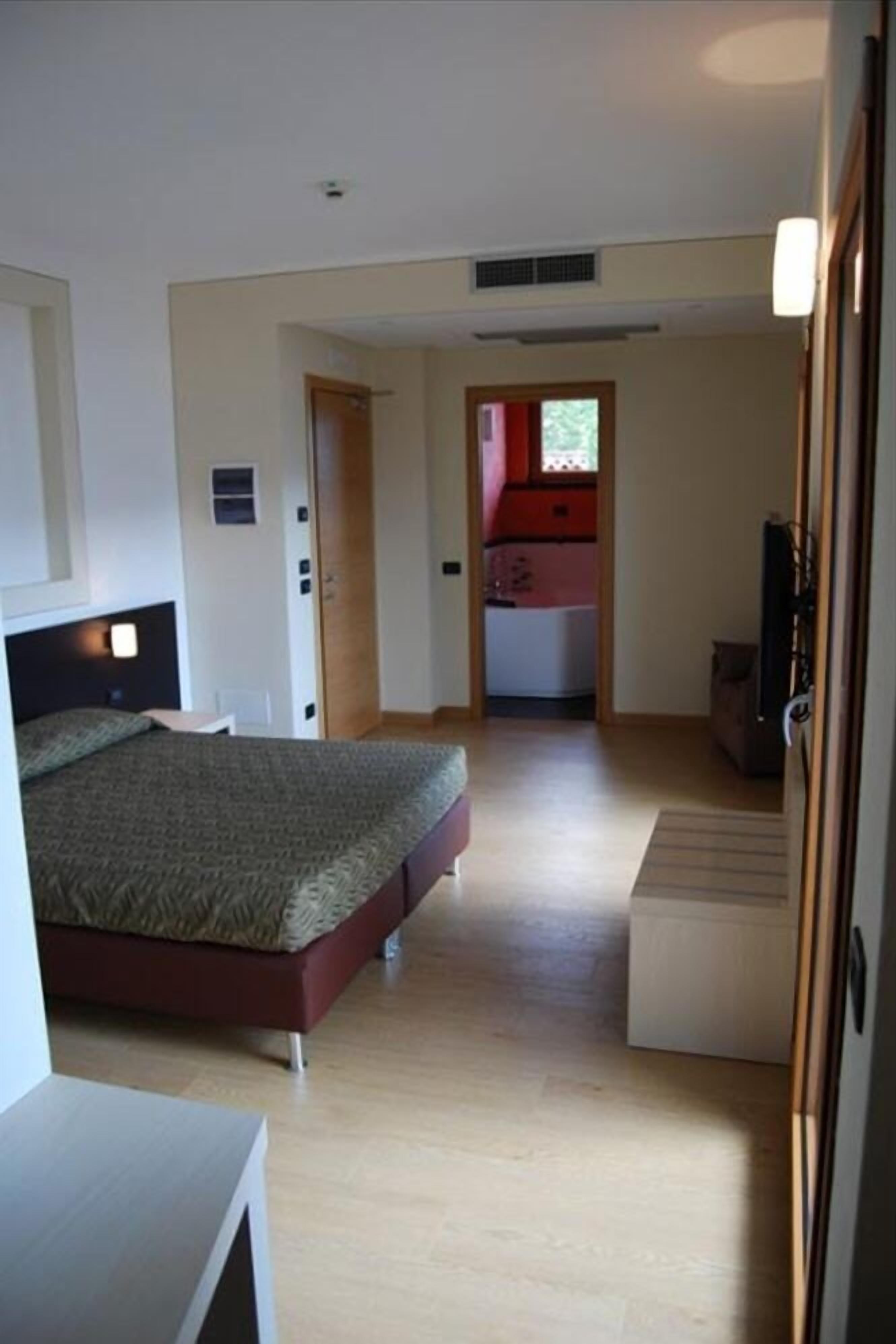 A bedroom with a bed, a desk, and a small kitchenette in the background.