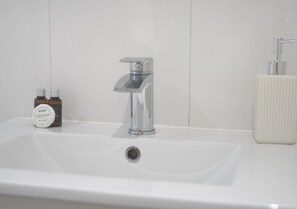 Ein Waschbecken mit chromfarbenem Wasserhahn, einer Seifenspender und zwei Seifenflaschen.