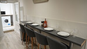 Un coin repas avec une longue table dressée pour quatre personnes, un tabouret de bar et un panneau sur lequel on peut lire : « Soyez nos invités. »