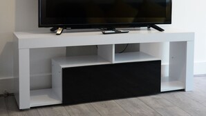 Un téléviseur à écran plat est posé sur un meuble blanc, avec une étagère en dessous.