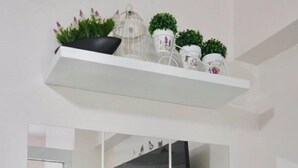 Een moderne kamer met een grote spiegel, een eettafel met stoelen en een plank met decoratieve spullen.