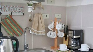 Een keuken met een spoelbak, waterkoker, koffiezetapparaat en mokken op een rek.