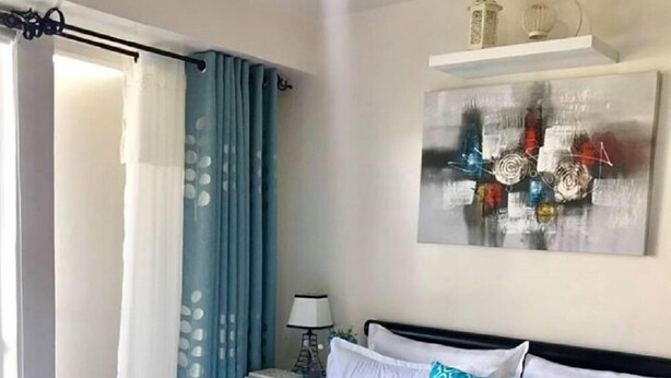 Een net opgemaakt bed met wit- en blauwe beddengoed, een kussen met blauw-wit patroon, en een klein decoratief object op het bed.