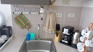 Een keuken met een spoelbak van roestvrij staal, een koffiezetapparaat en een set mokken op een houten standaard.