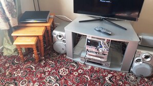 Un téléviseur posé sur un meuble, avec une télécommande, un ordinateur portable et une petite table.