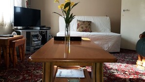 Un salon avec une table en bois, un téléviseur, un canapé et un coussin à motifs floraux.