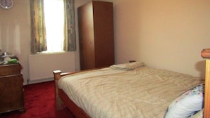 Une chambre à coucher avec un lit, une commode, un radiateur et une fenêtre avec des rideaux.