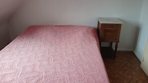 Une pièce avec un lit, une table de chevet en bois et un mur blanc.