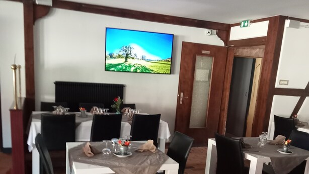 Un coin repas avec des tables disposées pour accueillir quatre personnes, un téléviseur fixé au mur et un sol en briques.