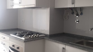 A kitchen with white cabinets, a gas stove, and a stainless steel sink. - Hostel Triúno (Lisbon)