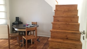 A room with a wooden staircase, a round dining table with chairs, and a door with a window. - Hostel Triúno (Lisbon)