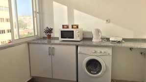 A compact kitchen with a microwave, coffee maker, and washing machine. - Hostel Triúno (Lisbon)