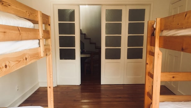 A room with two bunk beds, wooden flooring, and a white door with frosted glass panels. - Hostel Triúno (Lisbon)