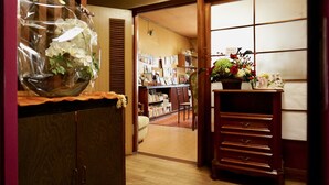Un intérieur japonais traditionnel avec des portes coulissantes en bois, un meuble en bois orné d’un vase en verre, et une bibliothèque remplie de livres et d’objets décoratifs.