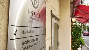 L’entrée d’un immeuble, avec une enseigne indiquant un hôtel nommé « tomaru.bldg » et un studio de danse.