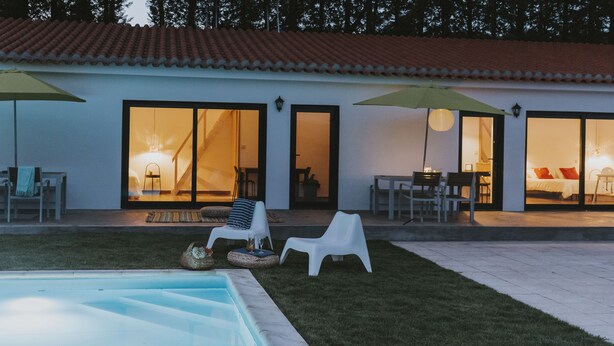 A poolside area with a clear view of the pool, a grassy lawn, and a building with large glass doors and windows. - Lugar nas Estrelas (Covilhã)