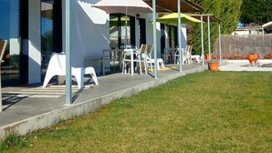 A covered outdoor seating area with chairs and umbrellas, a building with large windows, and a grassy lawn. - Lugar nas Estrelas (Covilhã)