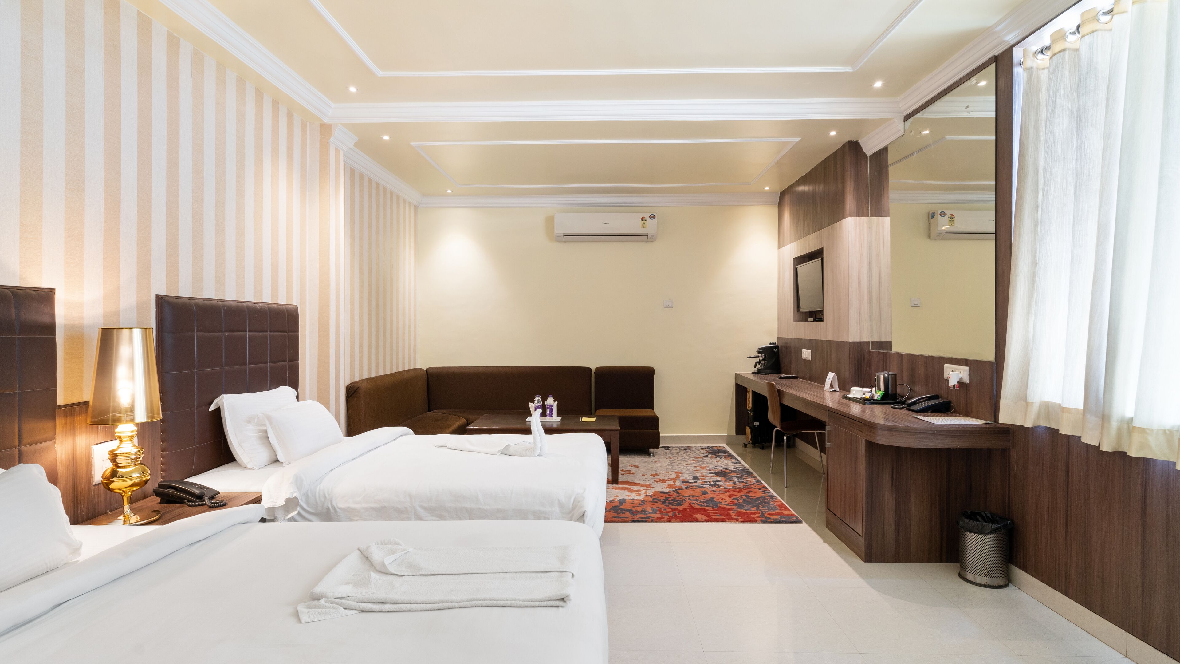 A hotel room with two beds, a sofa, a desk, a mirror, and a bathroom.