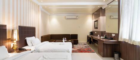 A hotel room with two beds, a sofa, a desk, a mirror, and a bathroom.