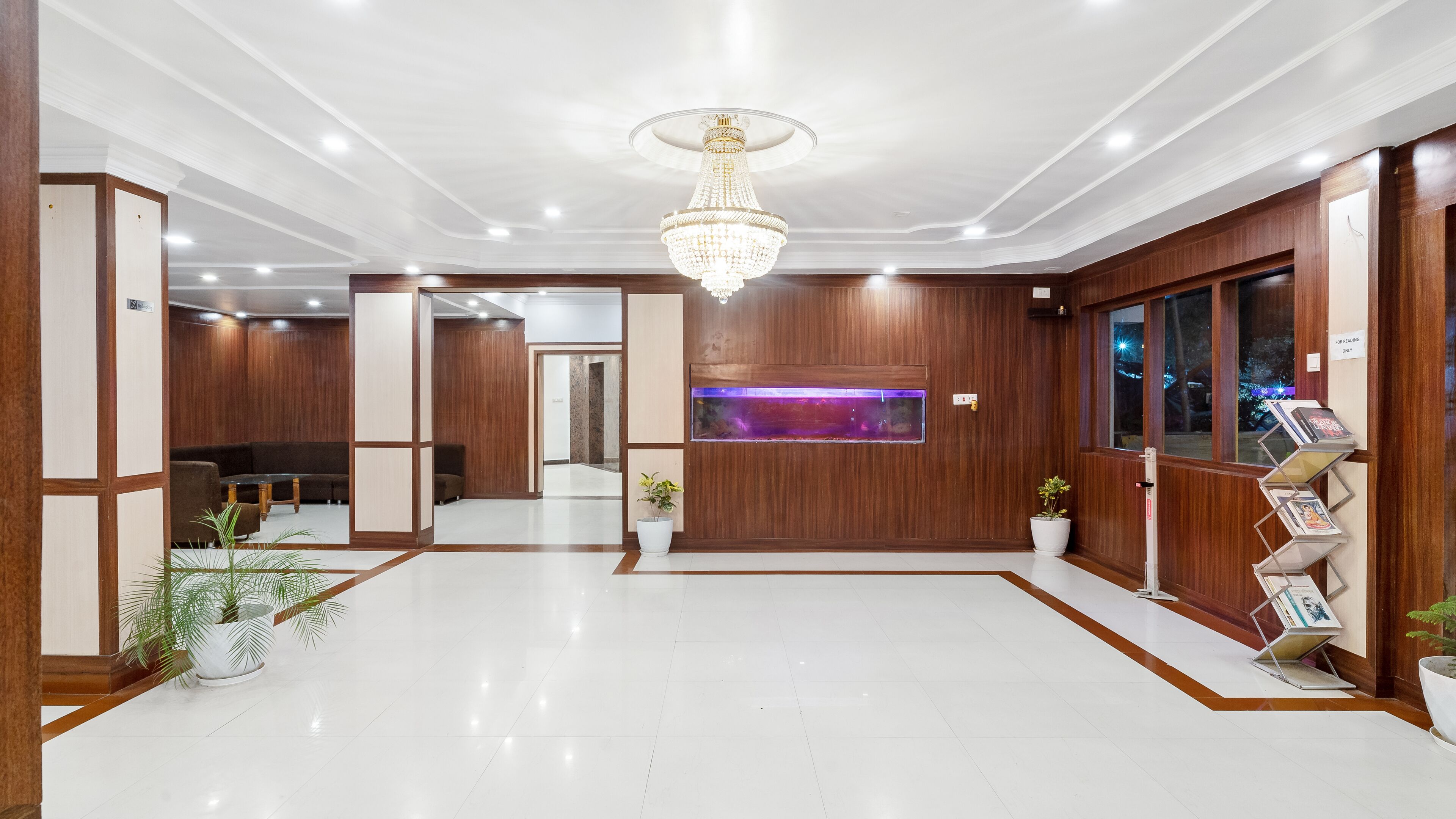 Um hall espaçoso com um candelabro, painéis de madeira, um balcão de recepção e um aquário.