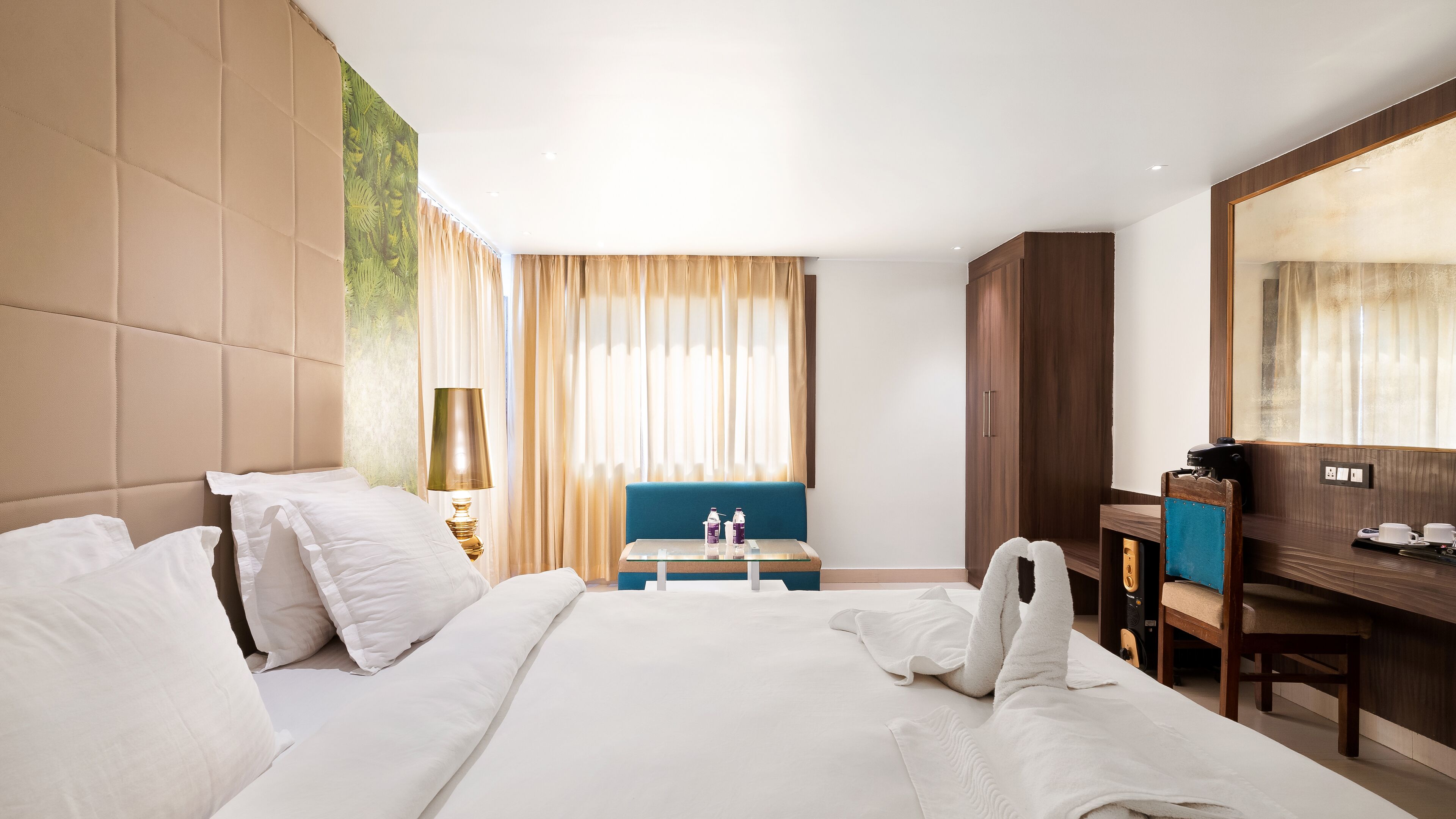 A hotel room with a large bed, a desk, a chair, and a wardrobe.