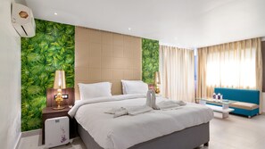 Une chambre d’hôtel avec un lit, deux tables de chevet avec des lampes, un canapé bleu, une table basse en verre et une fenêtre avec des rideaux.