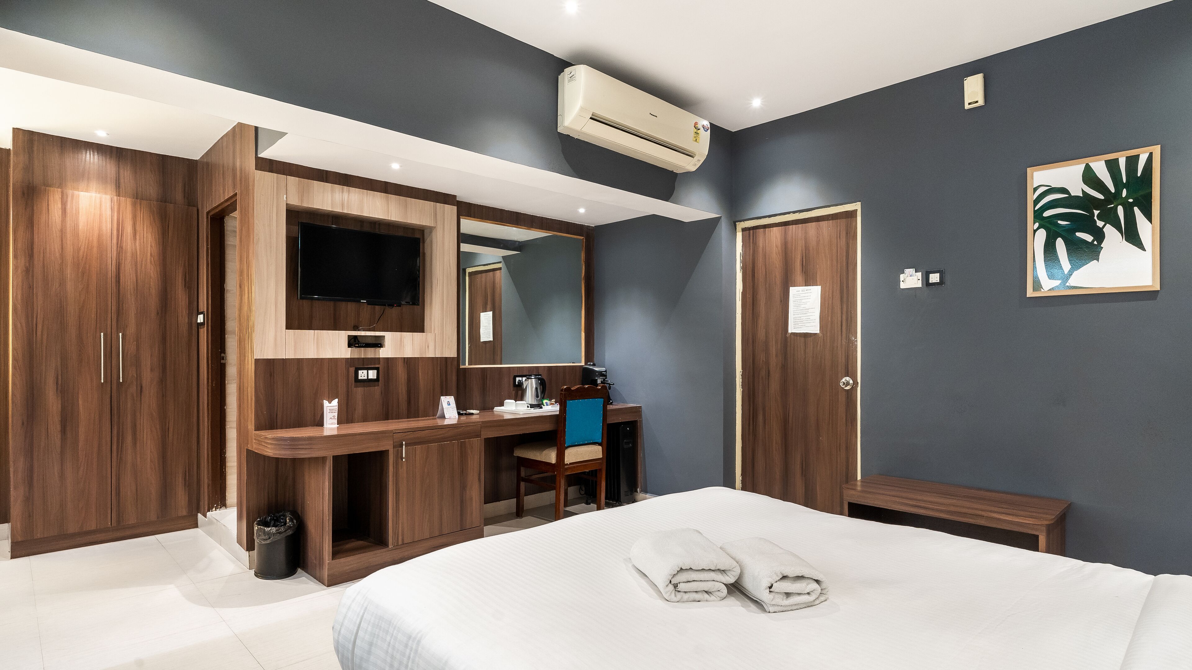 Une chambre d’hôtel équipée d’un lit, d’un bureau avec une chaise, d’un miroir, d’une télévision et d’un climatiseur.