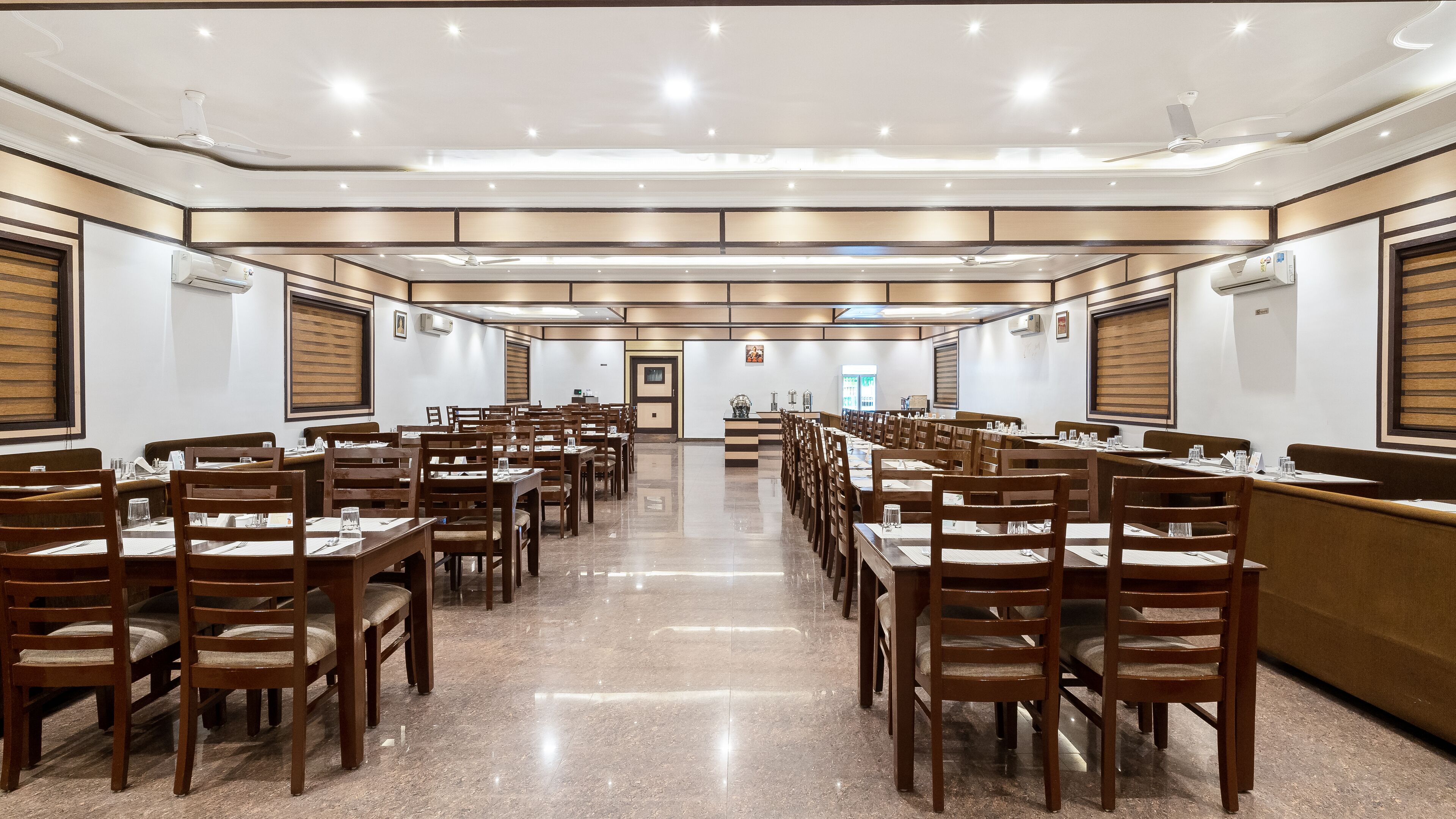 Une salle à manger spacieuse, dotée de nombreuses tables et chaises, de ventilateurs de plafond et d’un éclairage encastré.