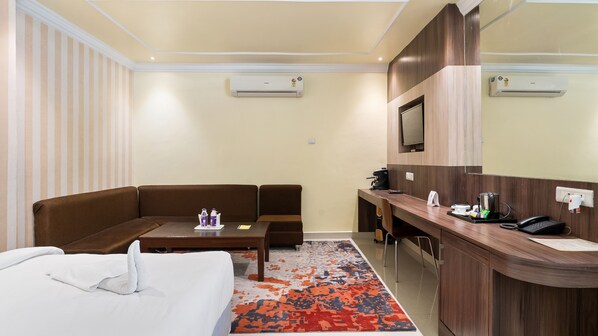Une chambre d’hôtel avec un canapé, une petite table avec des bouteilles d’eau, une machine à café, un bureau avec un téléphone et une télévision.