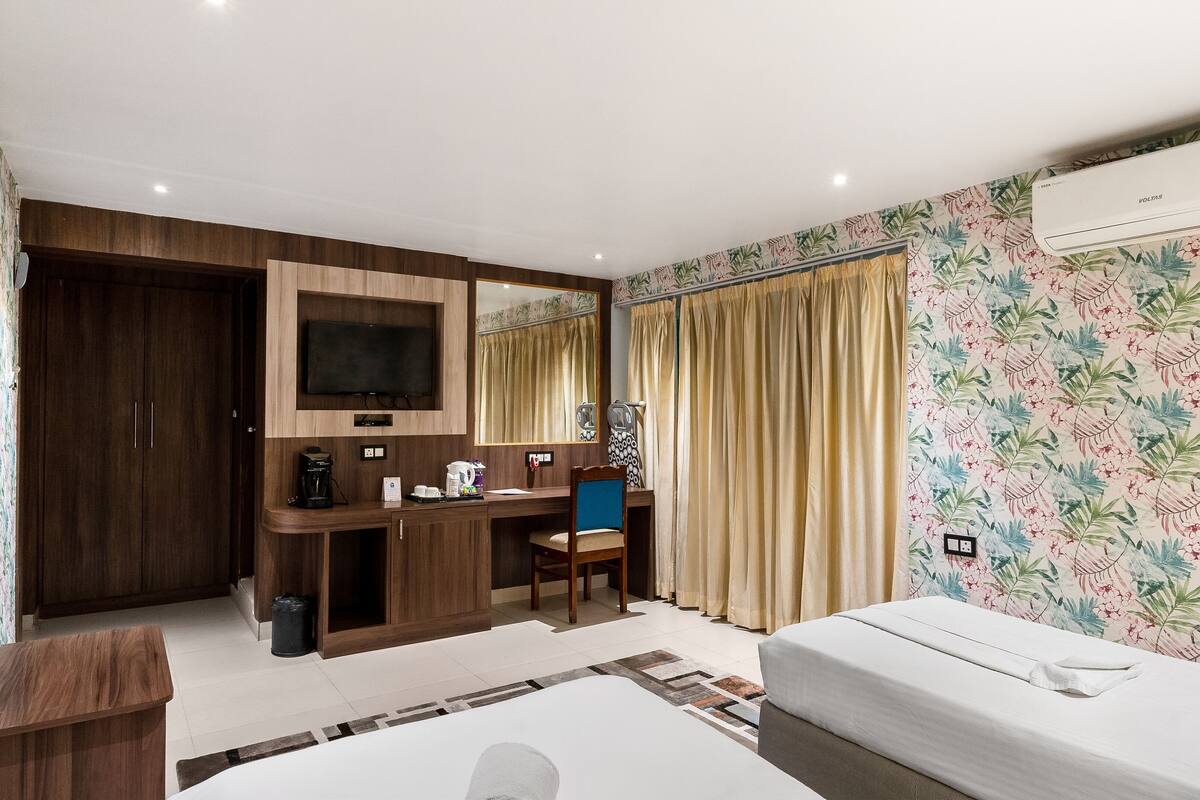 Een hotelkamer met een bed, een bureau met stoel, een televisie, een kledingkast en een airconditioner.