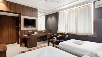 Una habitación de hotel con una cama, un escritorio con silla, un televisor y una ventana con cortinas.