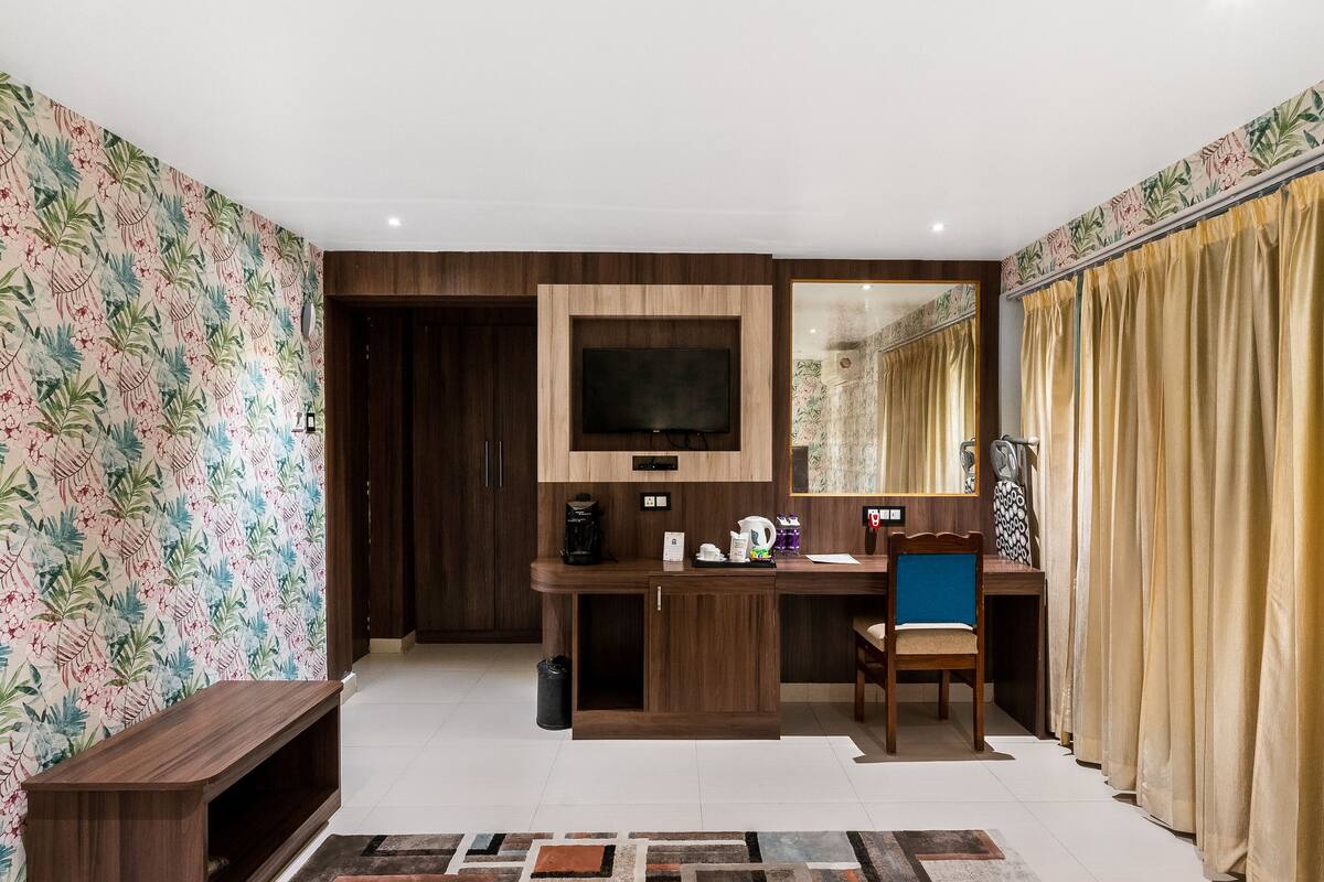 Een hotelkamer met een houten bureau, een televisie, een stoel en een groot raam met gordijnen.