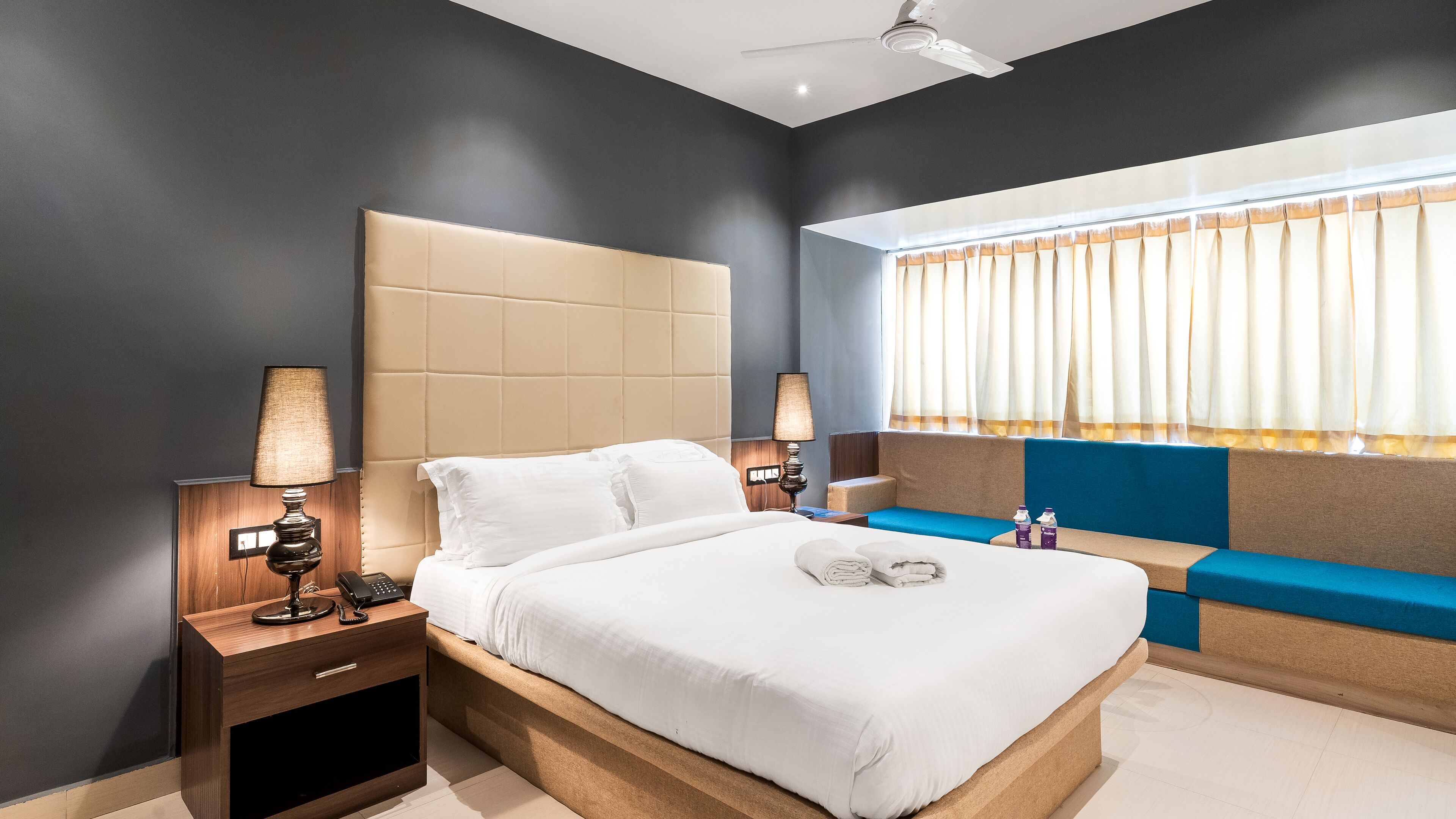 A modern hotel room with a large bed, bedside lamps, a built-in bench, and a window with curtains.