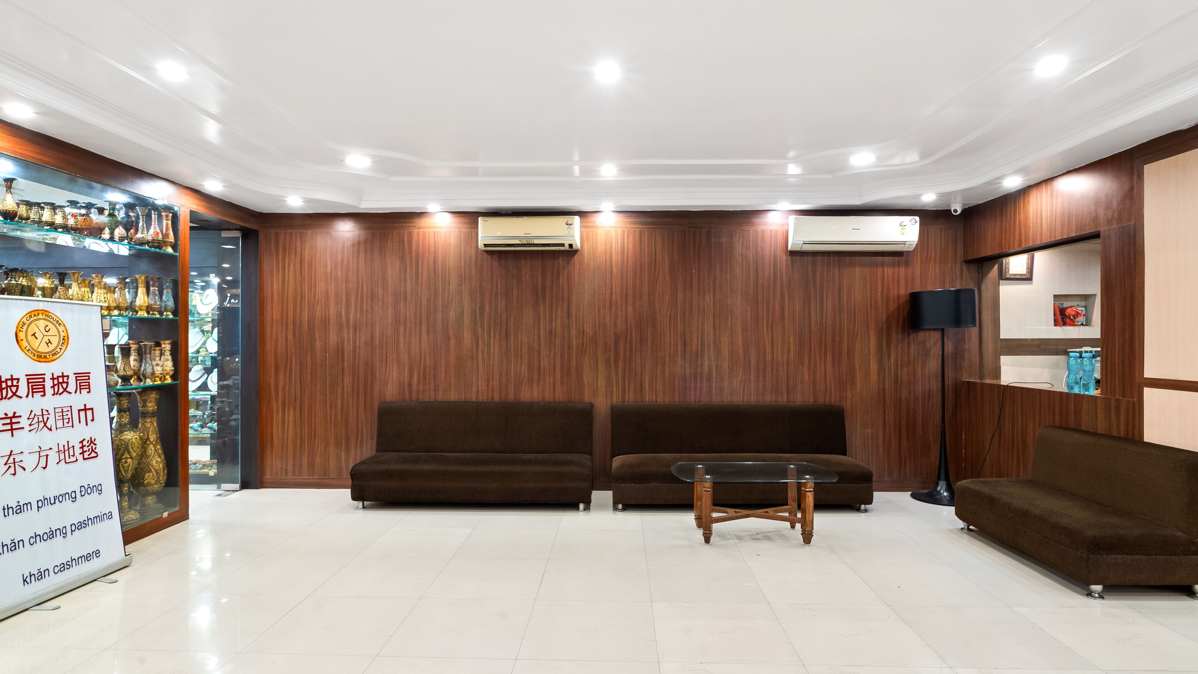Zona de recepción con paneles de madera, dos sofás, una mesa de centro y una exhibición de cerámica.