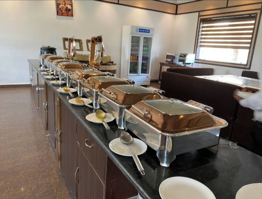 A buffet setup with multiple serving stations, a refrigerator, and a window with blinds.