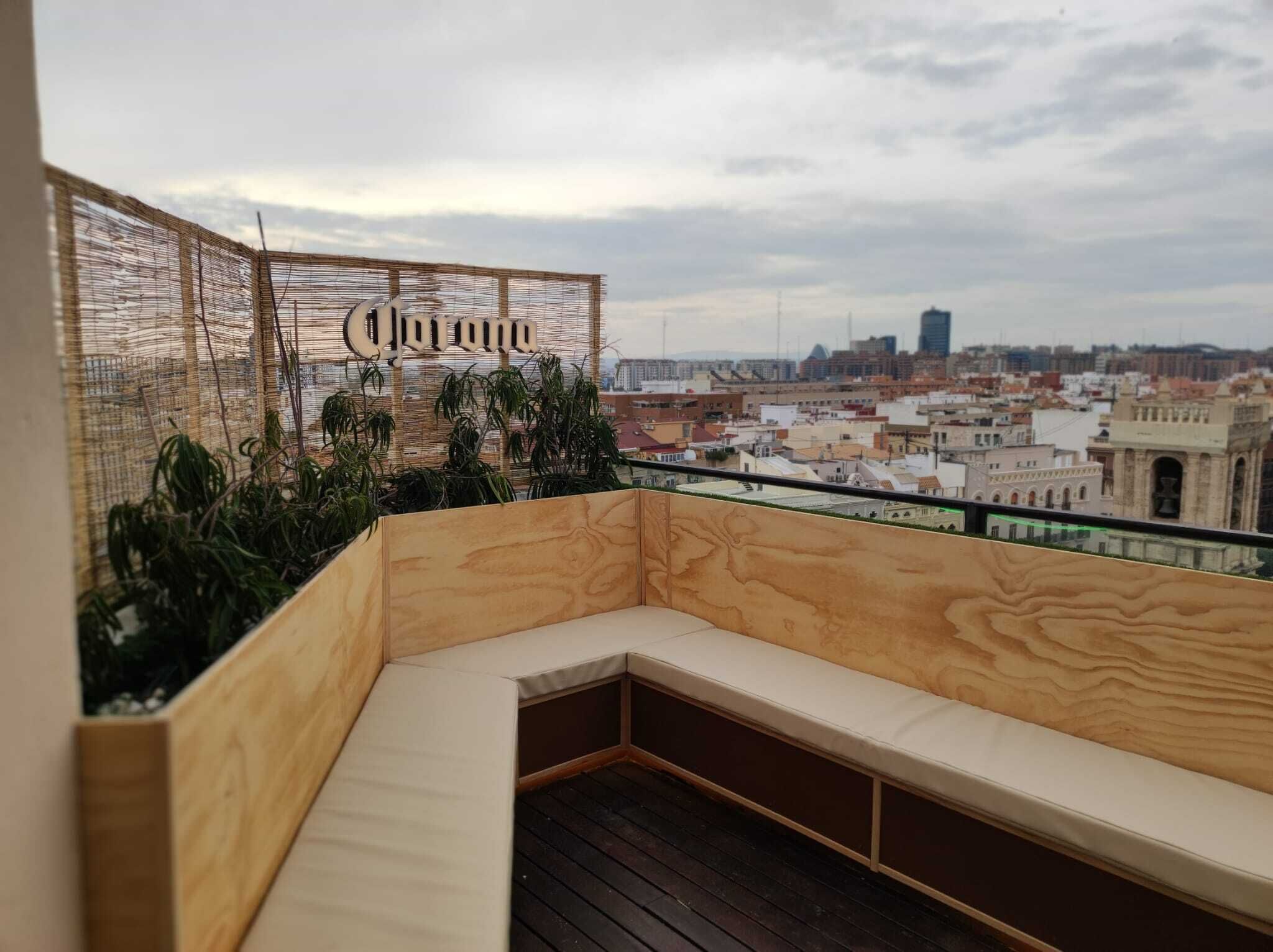 Um deck de madeira com um banco, cerca de tear e vista para a cidade.