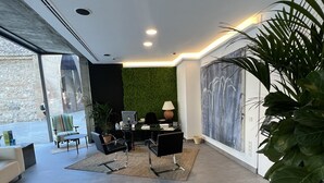 Una sala moderna con un ventanal grande, una pared verde y un cuadro. Hay dos sillones negros, una mesita y una planta en maceta.