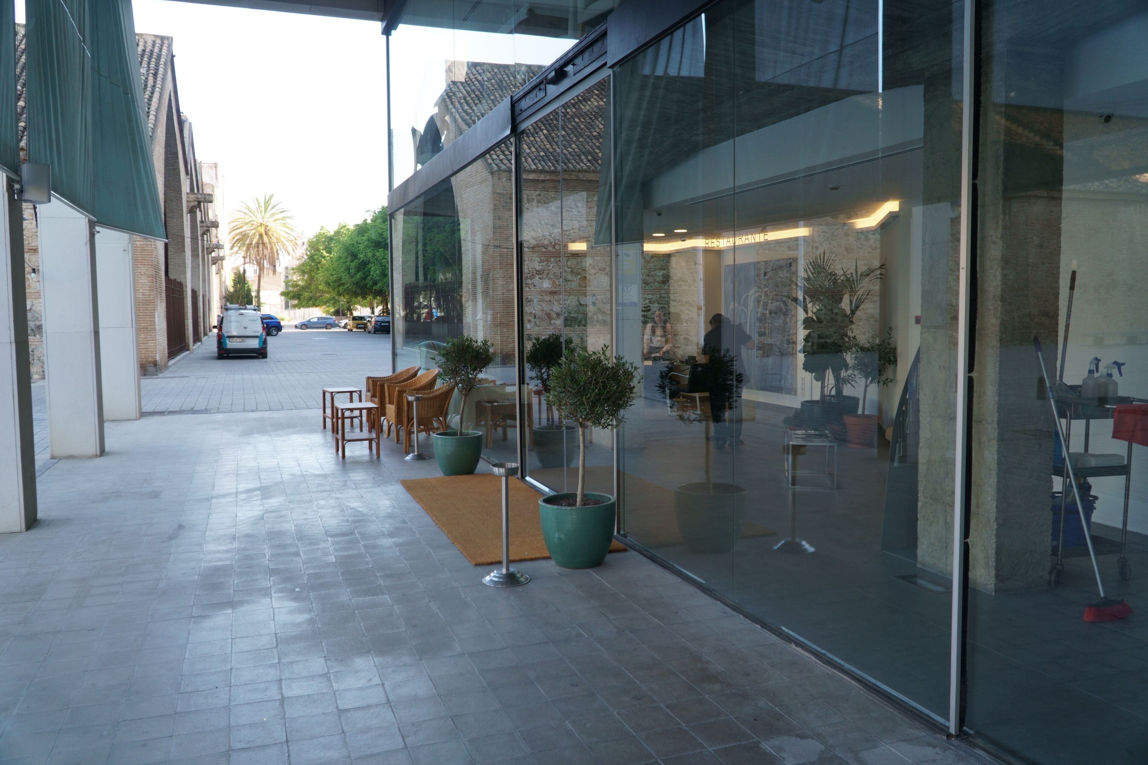 An outdoor seating area with tables and chairs, potted plants, and a glass storefront.