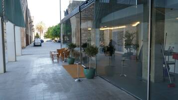 An outdoor seating area with tables and chairs, potted plants, and a glass storefront.