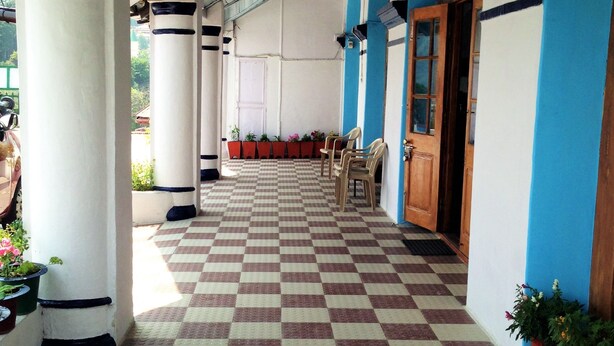 A covered corridor with checkered flooring, white pillars, and blue walls. - Prince Hotel (Dehradun)