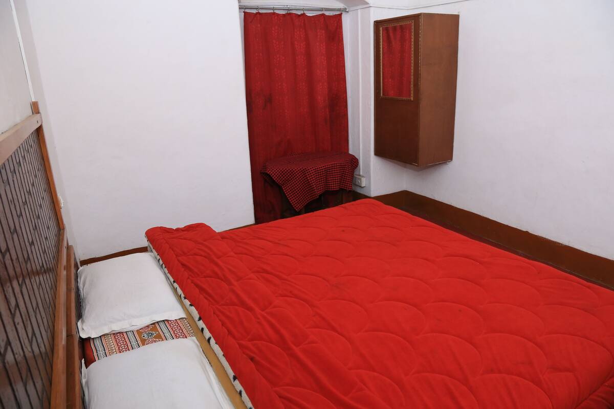 A small, neatly made room with a single bed, a small table with a checkered tablecloth, and a mirror on the wall.