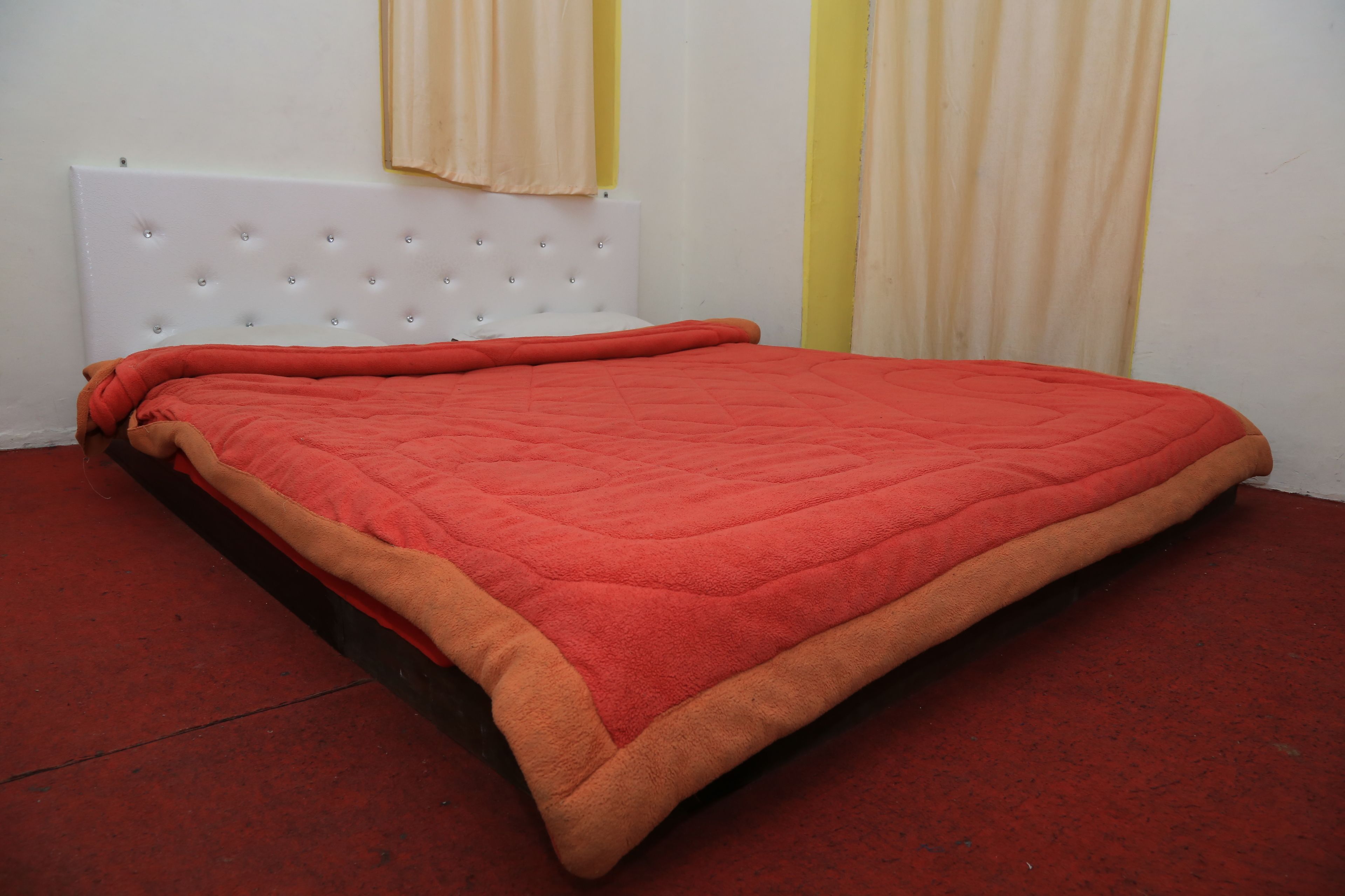A bed with a white headboard and a red blanket.